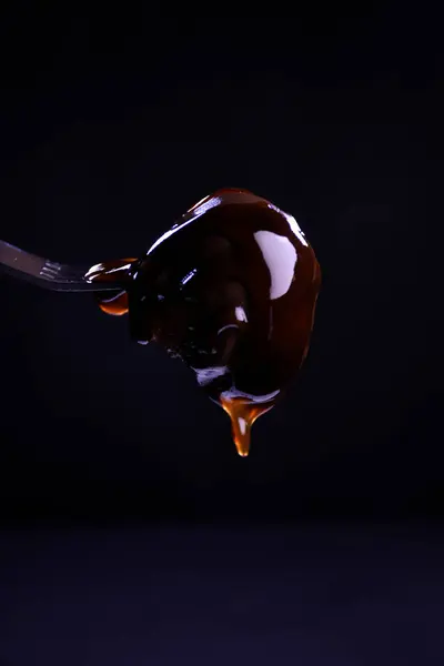 Profiteroller, siyah bir arka planda çatalla tutturulmuş kahverengi üzerine çikolata serpiştirilmiş ekler-