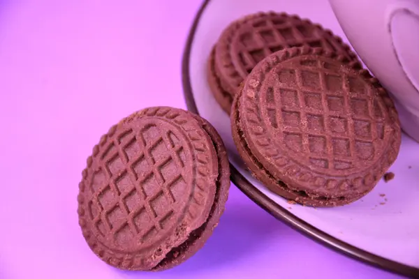 Pembe seramik fincanda çikolatalı kurabiye ve pembe arka planda çay tabağı.