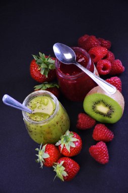 Bir kavanoz çilek reçeli ve siyah arka planda taze çilekli kivi reçeli. Büyükannenin hazırlıkları. Egzotik.