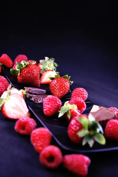 Meyve tabağı. Dikdörtgen bir tabakta çilek, ahududu ve çikolata parçaları.