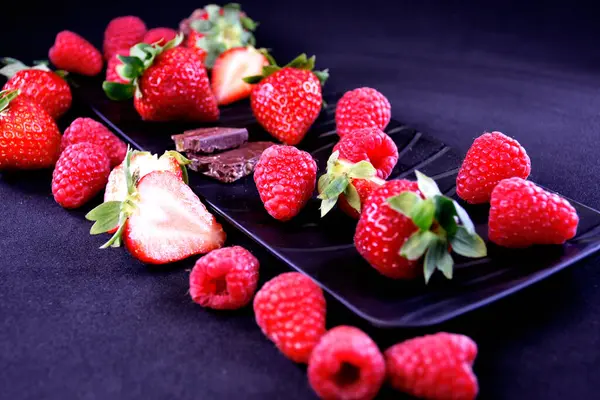 Meyve tabağı. Dikdörtgen bir tabakta çilek, ahududu ve çikolata parçaları.