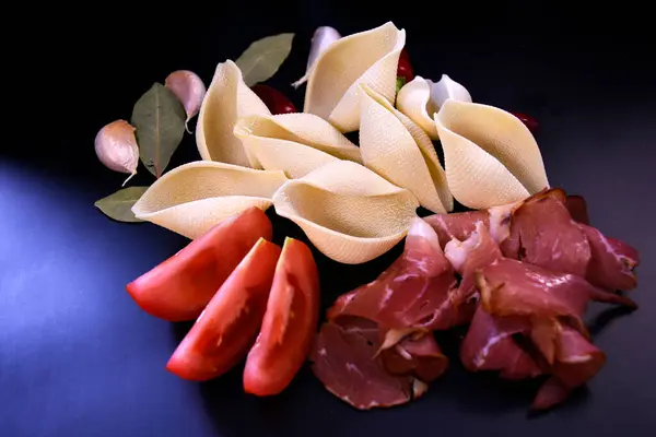 Taze domatesli makarna kabuğu ve siyah arka planda jambon. İtalyan mutfağı.