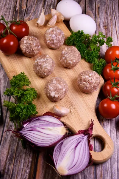 Masanın üzerinde taze sebzeler olan tahta kesme tahtası. Köfteler, pişmeye hazır köfteler. Salata için malzemeler. Yemek pişirme.