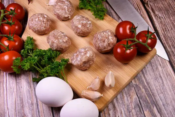 Masanın üzerinde taze sebzeler olan tahta kesme tahtası. Köfteler, pişmeye hazır köfteler. Salata için malzemeler. Yemek pişirme.