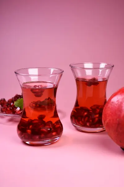 İki bardak nar suyu ve taze meyveler. Bir bardakta Türk nar çayı ve taze nar. Yüzeyde taze nane ve nar tohumları.