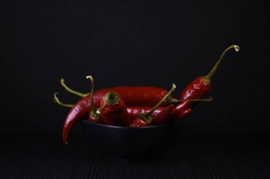 Siyah camda izole edilmiş taze kırmızı biberler. Siyah arka planda siyah tabakta acı kırmızı biber. Siyah arka planda hala hayat var. Parlak biber.