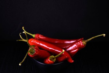 Siyah camda izole edilmiş taze kırmızı biberler. Siyah arka planda siyah tabakta acı kırmızı biber. Siyah arka planda hala hayat var. Parlak biber.