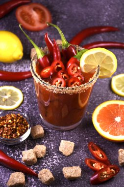 Baharatlı ve biberli cam bir kavanozda acı biber sosu. Acı biber ve limonla süslenmiş koyu bir arka planda Bloody Mary alkollü kokteyl. Yüzeyde biber, limon, çim şekeri.