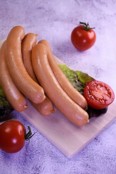 Ahşap masada domatesli sosisler. Kesme tahtasındaki sosisler, küçük domatesler. Gri arkaplan.