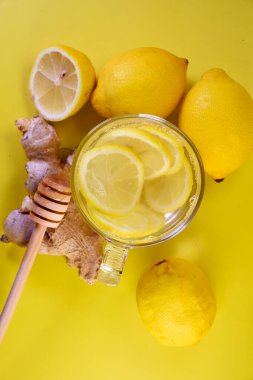 Limon ve ballı sıcak vitamin içeceği. Sarı arka planda sarı limonlar. Cam bardak..