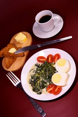 Sağlıklı kahvaltı. Çeri domatesli haşlanmış yumurta ve peynir soslu ıspanak. Kahve ve tereyağlı ekmek. Uygun beslenme.