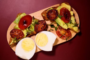 Avokado, yumurta, domates ve peynirli tost. Sağlıklı kahvaltı. Avokado ezmeli tost ve kızarmış domates, ahşap bir tahtanın üzerinde haşlanmış yumurta..
