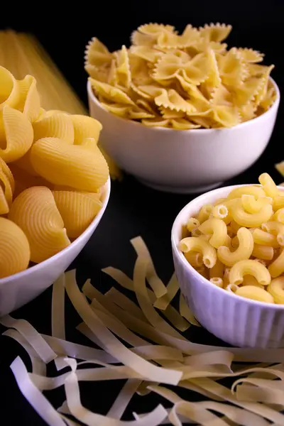 Siyah arka planda beyaz tabakta çiğ makarna. Yapıştırıcının desenli bir yüzeyi ve açık sarı bir rengi var. Makarna arkaplanı ve dokusu.