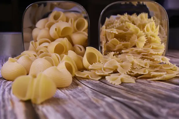 Cam kaplarda çiğ makarna ve ahşap zemine saçılmış. Yapıştırıcının desenli bir yüzeyi ve açık sarı bir rengi var. Makarna arkaplanı ve dokusu.