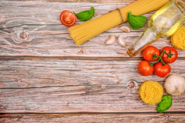 Tahta bir yüzeyde İtalyan makarnası pişirmek için malzemeler. Fotoğrafta sicimle bağlanmış spagetti, dalda taze domates, sarımsak, fesleğen yaprağı, bir demet ince vermicelli ve bir şişe zeytinyağı görülüyor..