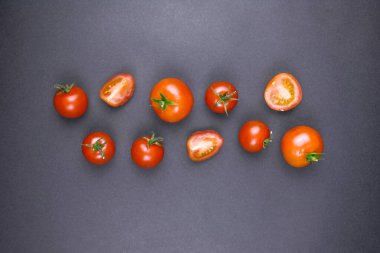 Taze kırmızı domatesler, bütün ve yarı yarıya, siyah arkaplanda dikey bir çizgi halinde dizilmiş.