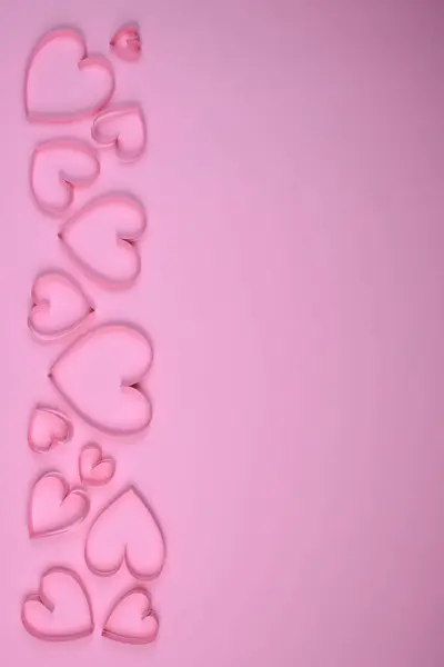 Farklı boyutlarda pembe kalpler düz pembe bir arka planda düzgünce serilmiştir..