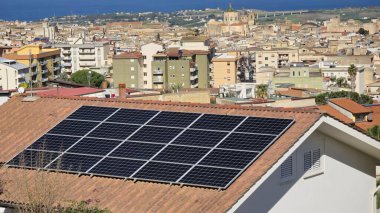 Tepeden Akdeniz 'in panoramik manzarası. Ön planda, çatılarında güneş panelleri bulunan ve yenilenebilir enerji kaynaklarının kullanımını sembolize eden konut binaları bulunuyor..