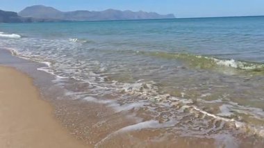 Gök mavisi denizin ve dağların arkasında küçük dalgalar oluşturan kumsal.