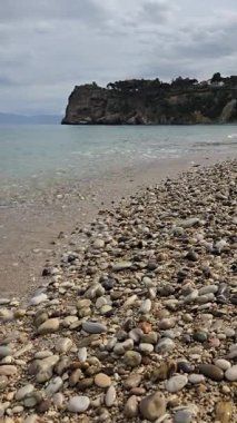 Gök mavisi denizin ve dağların arkasında küçük dalgalar oluşturan kumsal.