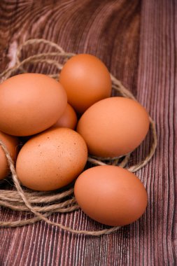 Kahverengi tavuk yumurtaları sert sicimle çevrili ahşap bir yüzeyde yatar..