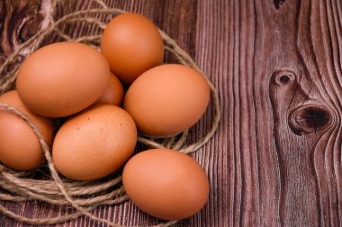Kahverengi tavuk yumurtaları sert sicimle çevrili ahşap bir yüzeyde yatar..