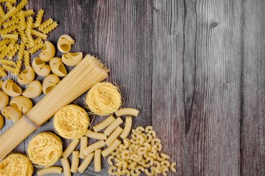 Ahşap arka planda makarna çeşitleri. Dikkatlice masaya spagetti, koni, kabuk, fusilli ve erişte yuvaları koyun..