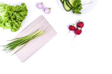 Beyaz arka planda taze sebzeler ve bitkiler. Tahta kesme tahtası, yeşil soğan, marul, turp, salatalık ve maydanoz..
