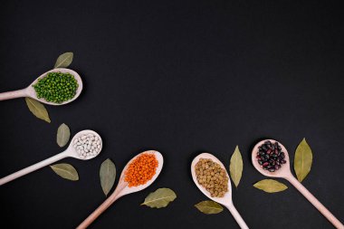 Koyu yapraklı, siyah arka planda tahta kaşıklarla çeşitli baklagiller. Sağlıklı besin maddeleri. Metin veya tasarım için kopyalama alanı olan minimalist kompozisyon.