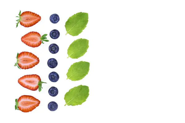 Taze çilek, yaban mersini ve nane yaprakları beyaz arka planda düzenli olarak sıralanmış. Canlı doğal renklere sahip minimalist kompozisyon. Sağlıklı yaz malzemeleri konsepti, menü tasarımı, yemek blogu veya ambalaj için mükemmel.