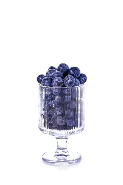 Beyaz arka planda izole edilmiş şeffaf cam bir kadehte taze olgun yaban mersini. Minimalist sağlıklı gıda konsepti. Temiz yemek, yaz meyveleri, antioksidan zengini abur cubur fikri.