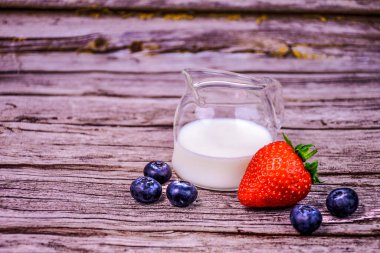 Taze çilek ve kremalı yaban mersini. Kır ağacında cam sürahi.