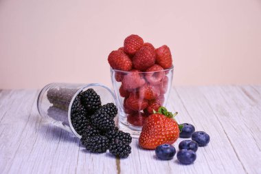Ahududu, böğürtlen, çilek ve yabanmersini de dahil olmak üzere taze karışık böğürtlen, kırsal ahşap arka planda cam bardaklarda sıralanmıştır. Sağlıklı gıda konsepti.