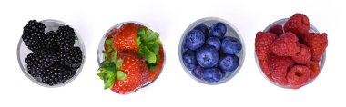 Beyaz arka planda cam kaselerde çeşitli taze böğürtlenlerin üst görüntüsü. Böğürtlen, çilek, böğürtlen ve ahududu. Minimalist sağlıklı besin bileşimi, izole ve düz..