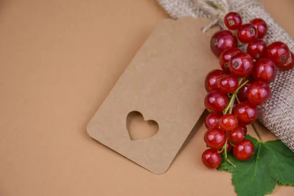 Taze kuşüzümlü yaz aranjmanı, çuval bezi rulosu, yeşil yaprak ve kesilmiş kalple birlikte el işi kağıt hediye etiketi. Çevre dostu ambalaj, el yapımı hediyeler, sıfır atık, yaz dekorasyonu veya romantik selamlama kavramı.