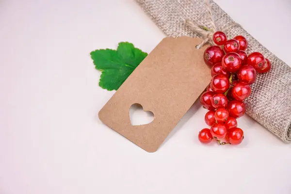 Doğal arka planda kesilmiş kalp ve kırmızı frenk üzümü içeren boş kraft kağıt etiketi