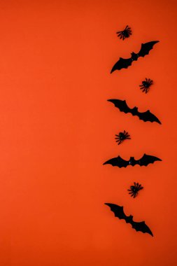 Minimalist bir Cadılar Bayramı tarzı kompozisyon: yarasa ve örümceklerin siyah silüetleri parlak turuncu bir arka plana karşı dikey olarak sağ tarafta dizilir.