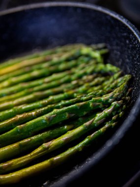 Bir adam tavada kuşkonmaz pişirir.