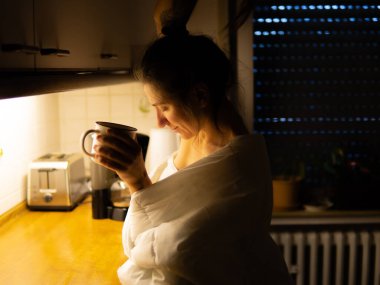 Bir kız mutfakta beyaz bir battaniyeyle kahve içiyor. Yüksek kalite fotoğraf