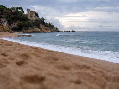 Deniz dalgaları kumlu sahilde, kayalara vuruyor. Denizde bir yelkenli. Mavi denizin üzerinde bir güvercin gökyüzü. Yüksek kalite fotoğraf