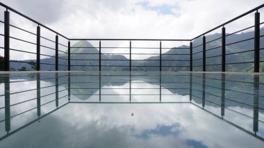 The glass bridge is a photo spot at Lombok cafe with views of the city and Mount Rinjani and green hills clipart