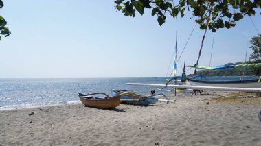 Two traditional boats placed on the beach facing the sea during the day with leaves on it at the Pasir Putih beach area of Situbondo