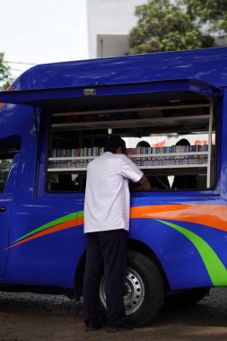 Malang şehrinin ortasında bir okur yazarlık alanında bir araba (mobil kütüphane) kitap rafını düzenleyen bir adam