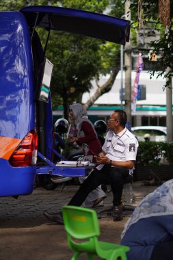 Malang şehrinin ortasında bir erkek kütüphane görevlisi bir arabanın yanında dinlenmek için oturuyor.