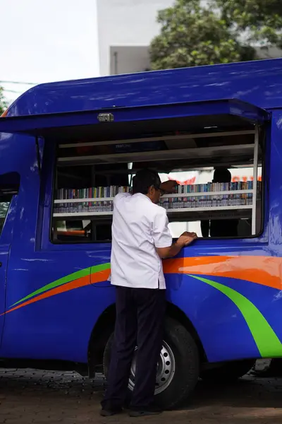 Malang şehrinin ortasında bir okur yazarlık alanında bir araba (mobil kütüphane) kitap rafını düzenleyen bir adam