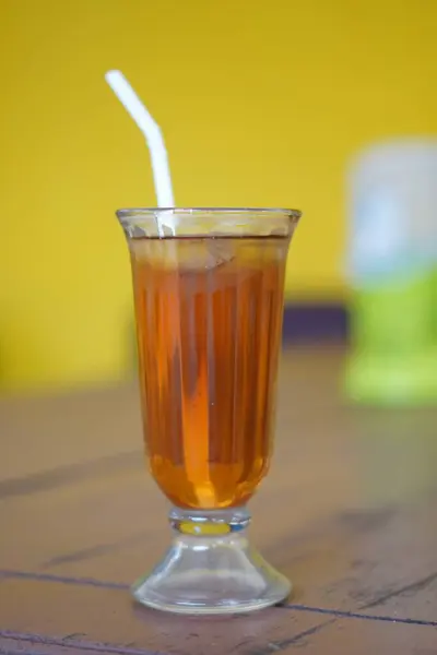 Bir bardak buzlu çay, berrak bir bardak, beyaz bir pipet ve bulanık bir arka plan.