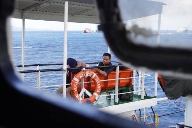 Geminin dışında oturan feribot yolcuları sabah deniz manzarasına bakarlar.