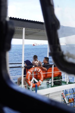 Geminin dışında oturan feribot yolcuları sabah deniz manzarasına bakarlar.