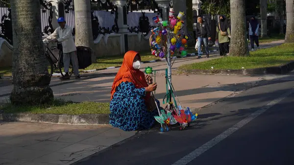 stock image A woman wearing an orange hood sits and sells children's toys on the side of the road in Malang's Car Free Day area to survive