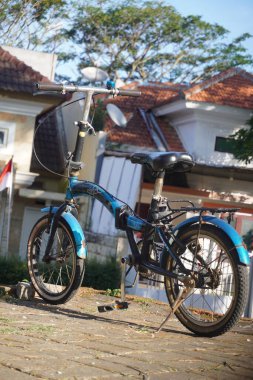 Evlerin bulanık arkaplanlı olduğu parka park edilmiş mavi bir bisiklet.
